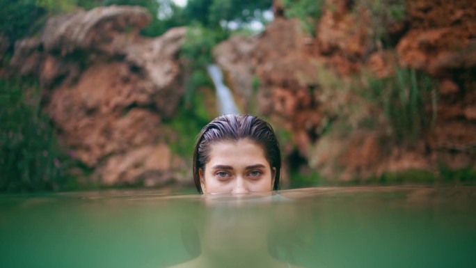 在荒野中偷窥水面的女人特写。湿发黑发游泳