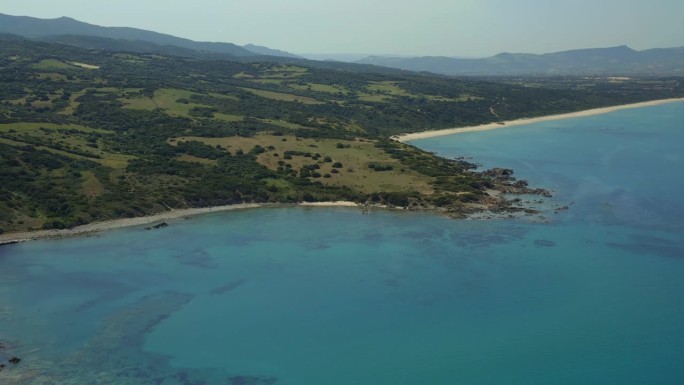 无人机的原始撒丁岛海岸线与充满活力的蓝色海水，岩石海岸，和郁郁葱葱的绿色景观，展示了意大利的自然之美