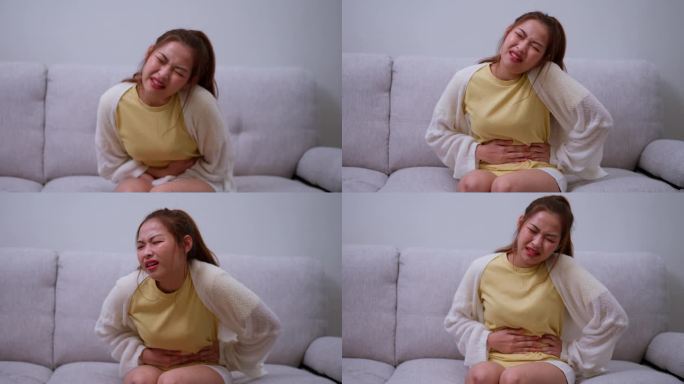 患病的亚洲妇女因经期(经前症候群)而腹部剧烈疼痛。坐在沙发上，食物中毒引起胃痛，腹痛，消化问题，胃炎