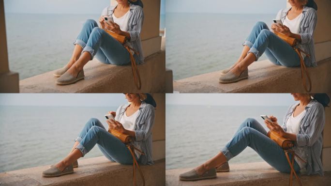 克罗地亚，一名女游客坐在海边的挡土墙上使用智能手机
