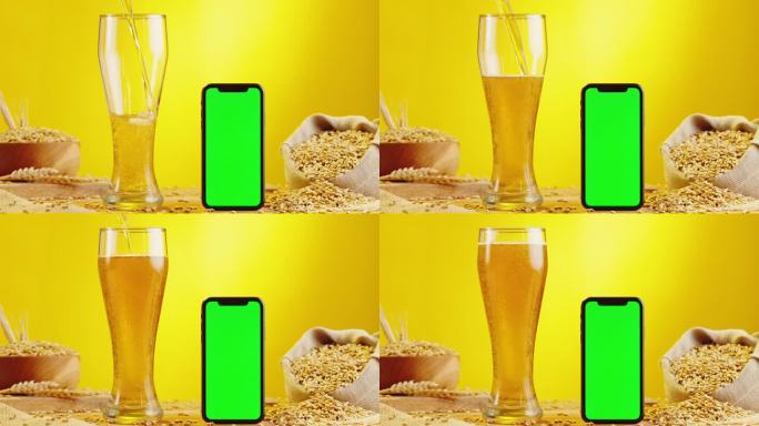 泡沫啤酒在玻璃和手机与绿色色度键屏幕。酒精金色啤酒杯喝。黄色背景下新鲜的淡色麦酒。