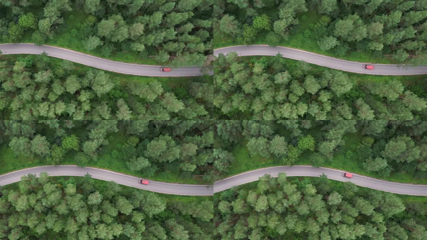 鸟瞰图夏日，红色汽车行驶在柏油路上，穿过广阔的森林。汽车在松林道路上行驶的航拍照片。穿越森林的公路旅