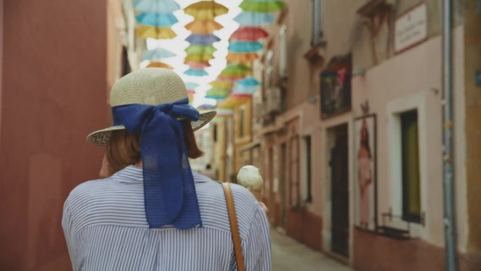 一名女游客戴着墨镜，吃着新鲜的甜筒冰淇淋走在克罗地亚村庄的街道上
