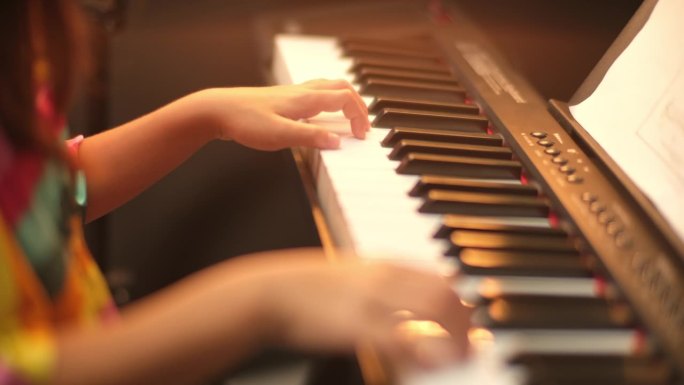 一个小学生弹钢琴的特写镜头。快乐的年轻亚洲女孩学习和练习钢琴。有选择性的重点。