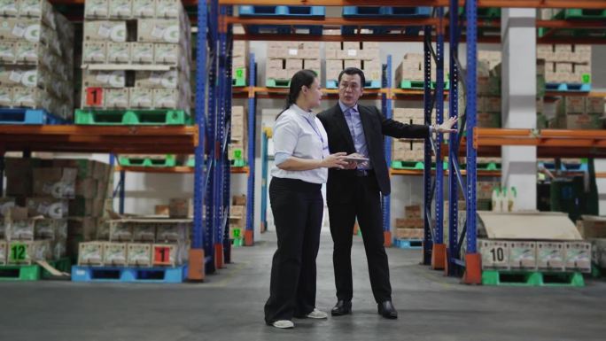 亚洲仓库管理人员在仓库用数码平板电脑进行讨论