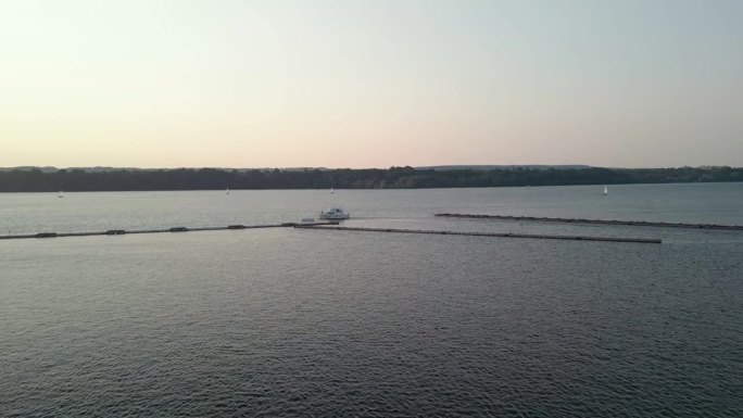 安大略湖的日落，广阔的蓝色水面荡起涟漪，一艘白色的游艇在画面的左边行驶，在它的路径上留下了一个小的尾