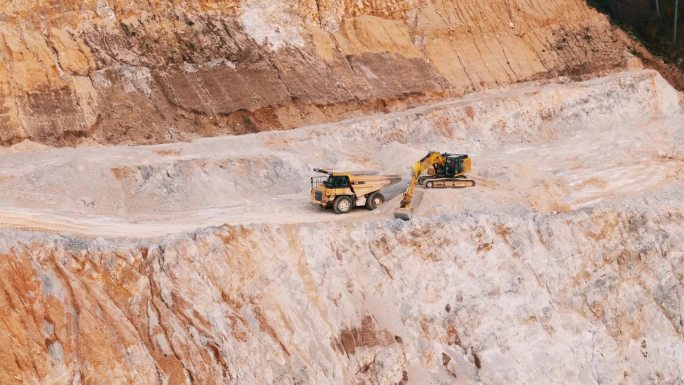 空中无人机拍摄的挖掘机装载矿物到露天矿坑自卸卡车