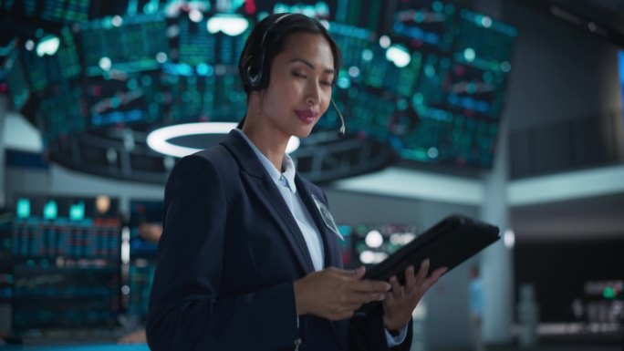 成功的女银行家在镜头前摆姿势，微笑。亚洲证券交易所经理使用平板电脑，戴着带麦克风的耳机与业务伙伴沟通
