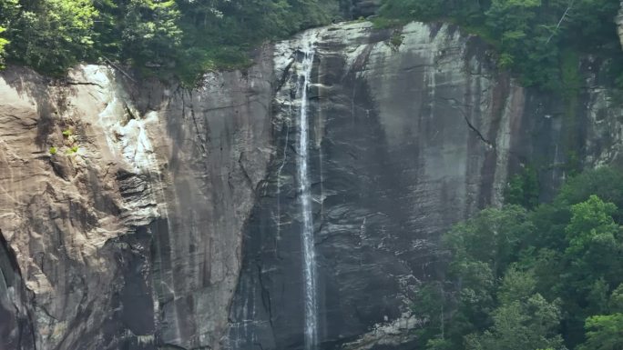 在美国北卡罗莱纳州的烟囱岩州立公园，山核桃仁从绿色茂密的树林之间的岩石巨石上落下清澈的水