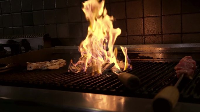 厨师在厨房烤架上明火烹调肉类特写。美味和多汁的肉烤烤鸡慢动作。准备烧烤食物的厨师。新鲜的烧烤餐在燃烧