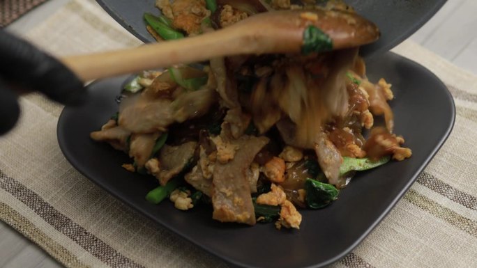 泰国街头小吃，厨师正在把看起来很美味的泰式酱油炒面(Pad See Ew)倒进盘子里