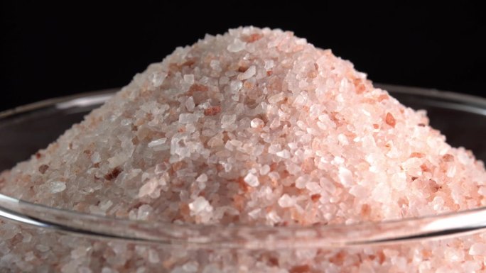 粉红色喜马拉雅盐或岩盐旋转在玻璃碗侧光。微量矿物质盐用于烹饪和食物展示，装饰灯和水疗