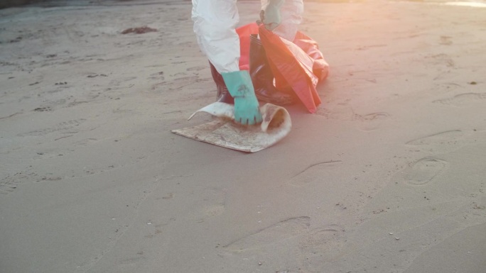 污染控制小组的个人防护用品用刷子清洁海滩上岩石上的石油泄漏
