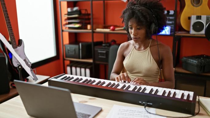 非洲裔美国女音乐家在音乐工作室用笔记本电脑弹钢琴