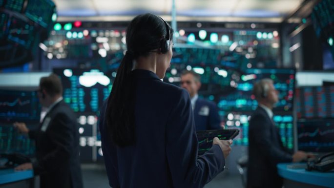 成功的证券交易所经理戴着耳机，在现代化的办公室工作。积极主动的女交易员在平板电脑上浏览财务报告，使用