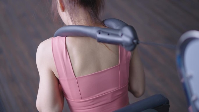 一个扎着马尾辫、穿着运动服的女士的后视图，在健身房独自做着坐着的拉线动作