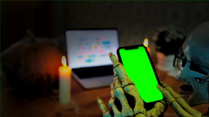 庆祝节日，死亡，骨手触绿色智能手机屏幕，可怕的万圣节背景