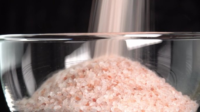 粉红色喜马拉雅盐或岩盐倒在玻璃碗。微量矿物质盐用于烹饪和食物展示，装饰灯和水疗