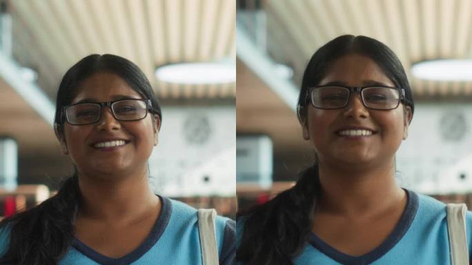 竖屏:一个快乐的印度学生站在传统公共图书馆的肖像。年轻的南亚女性看着镜头，微笑着。学者持有学术STE