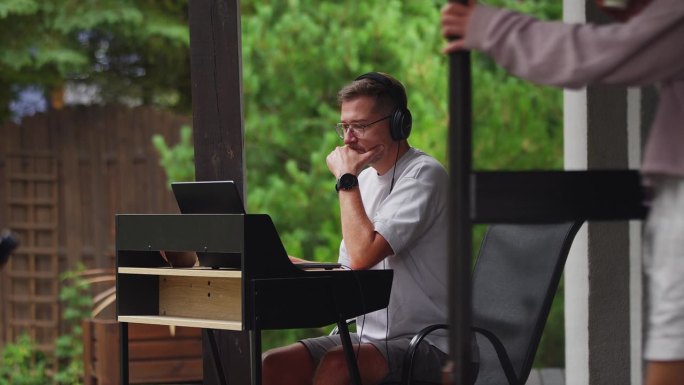 在户外工作。男人戴着耳机听音乐，盯着电脑屏幕