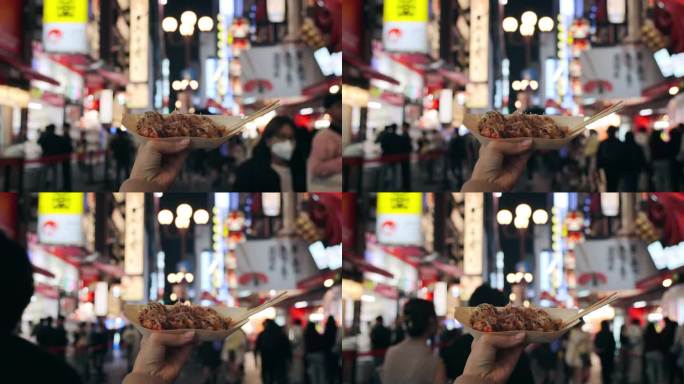 在大阪市中心的街道上，一名女游客正拿着新鲜制作的日本传统街头小吃章鱼烧(章鱼球)。镜头从她的个人角度