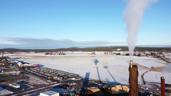 烟囱散发出灰白色的烟雾，在工业区后面的雪地上投下长长的影子