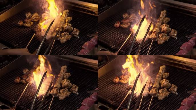 厨师在厨房烤架上明火烹煮鸡肉特写。美味多汁的肉烤在烤架上慢动作。准备烧烤食物的厨师。新鲜的饭菜在燃烧