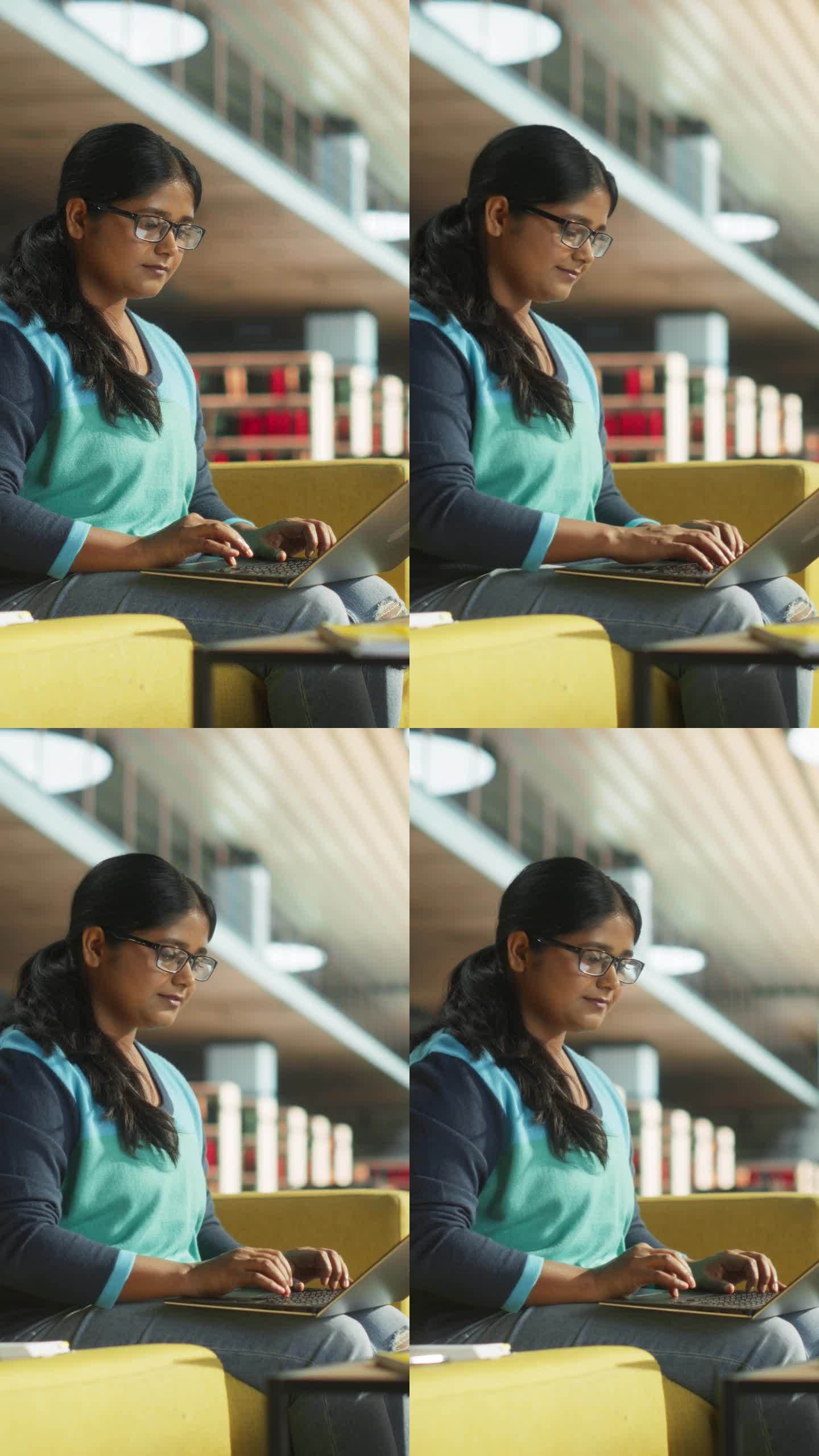 垂直屏幕:印度女性在公共图书馆使用笔记本电脑完成大学项目的课堂作业。年轻的南亚妇女在做练习的同时在线