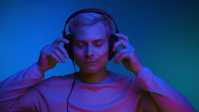 在室内拍摄的霓虹灯下，戴着耳机听音乐的人的肖像。一个时髦的家伙听到网络播放器的在线音频。时髦的模特在