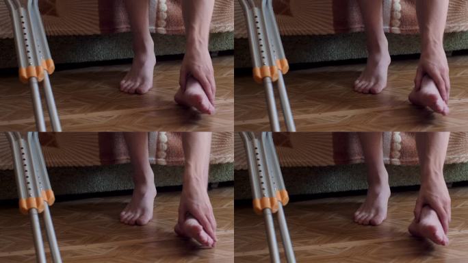 一名男子拄着拐杖坐在沙发上，在拆除石膏后触摸按摩骨折后疼痛的腿。四肢骨折后的康复。是健康的