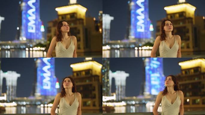 一名女子晚上走在迪拜哈利法塔和迪拜喷泉附近