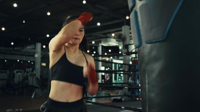 年轻的女拳手训练出拳，打沙袋，在拳击馆训练一天，力量强健身体，女孩打得快。