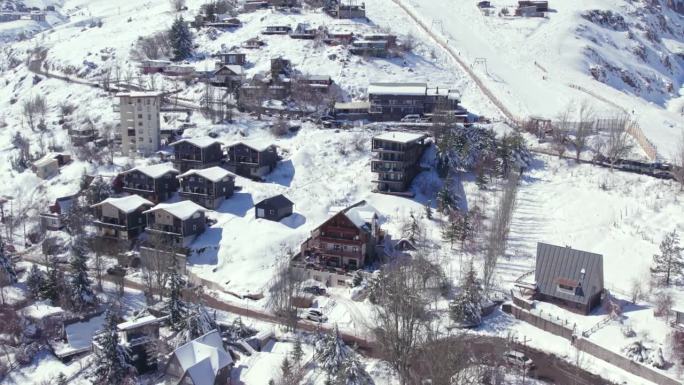 在智利一个阳光明媚的下雪天，一架绕轨道飞行的无人机拍摄了白雪覆盖的Farellones村庄的欧式房屋