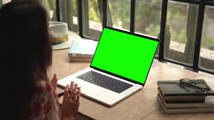 女人在笔记本电脑上工作，看着绿屏模拟色度键和视频通话。远程办公和讨论聊天特写。观看视频通话或阅读We