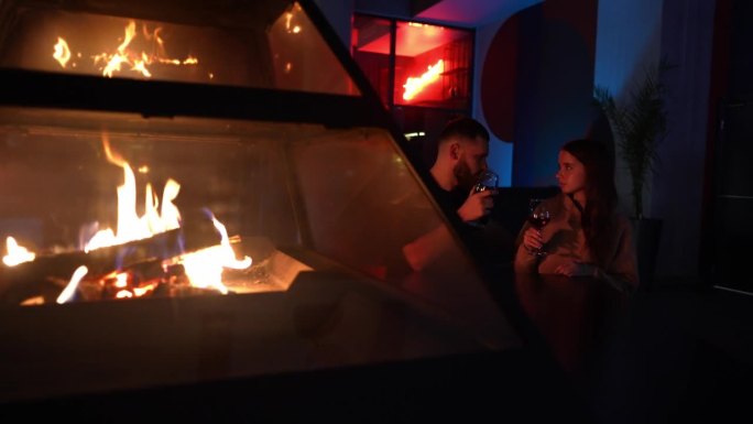 一对浪漫的情侣坐在壁炉旁，喝着红酒