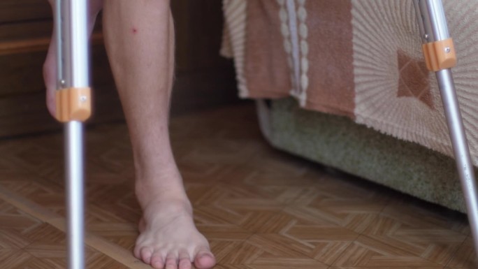 一个人拄着拐杖，腿上贴着石膏，在房子里走来走去。暂时性残疾腿骨骨折。健康理念
