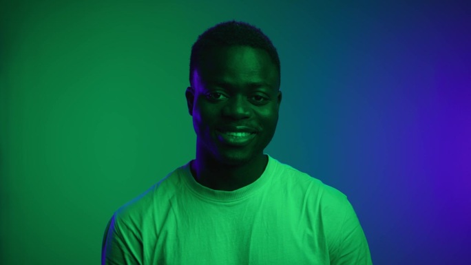 霓虹彩光下黑人看镜头微笑的快乐肖像。非裔美国人特写与迷人的白牙咧嘴。很酷的模型在真实的拍摄里面摆姿势