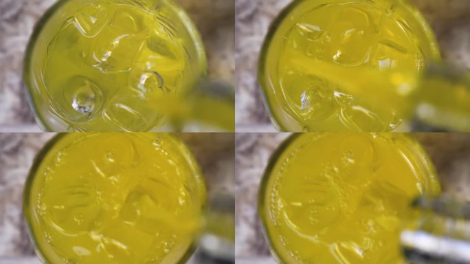 将一种类似橙汁的黄色液体倒入装有冰块的玻璃杯中。制作冷饮或酒精鸡尾酒的概念。