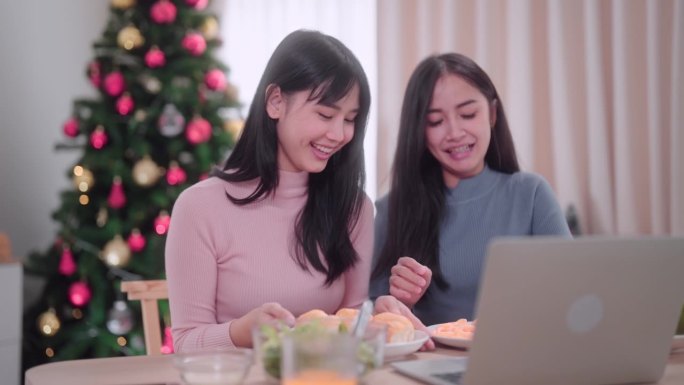 亚洲女性朋友通过笔记本电脑视频通话，在她家的餐桌上与朋友聊天庆祝圣诞节。抓住节日的联系和庆祝。