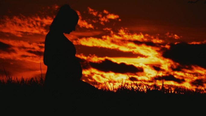 孕妇的剪影坐在戏剧性的日出天空
