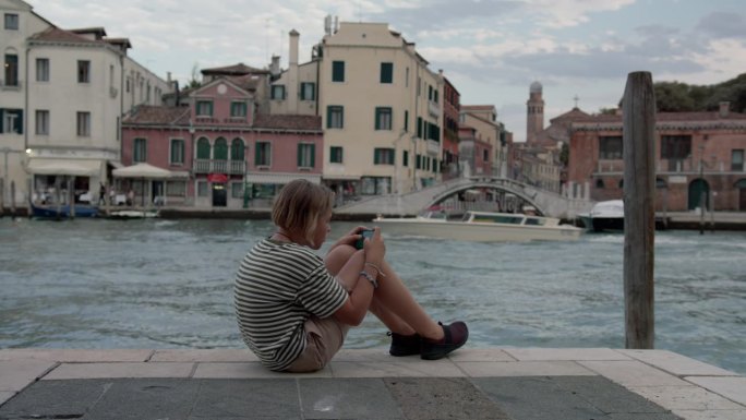 少年在威尼斯水边使用手机