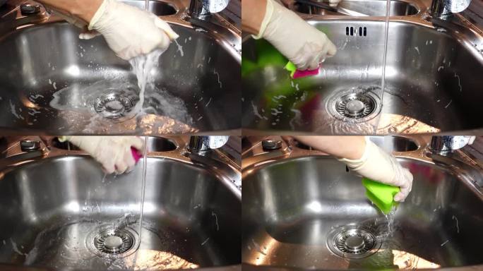 一位妇女小心地冲洗洗碗海绵和洗涤液。紧紧戴着手套的手把海绵从泡沫中拧出来。