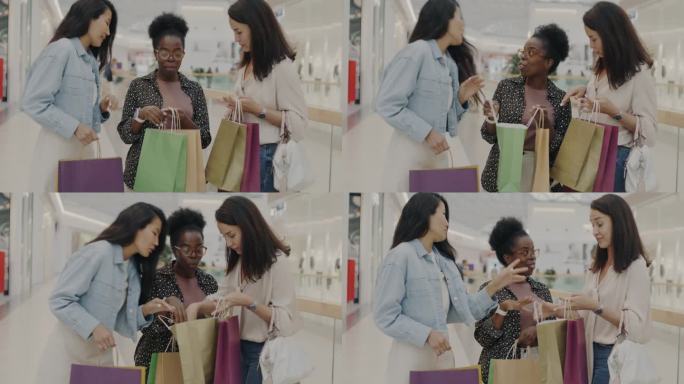 快乐的朋友看着购物袋里的新东西聊天，在现代商场里玩得很开心