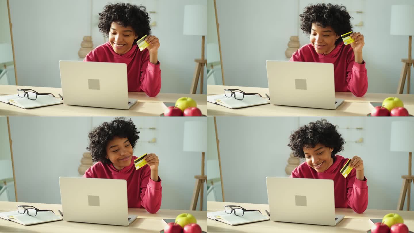 非裔美国妇女用笔记本电脑网上购物，用金卡支付。女孩坐在家里网上购物，输入信用卡信息。网上购物电子商务
