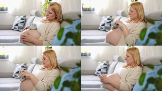快乐的孕妇，肚子上放着婴儿靴，躺在沙发上