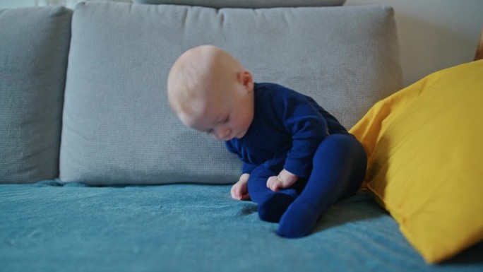 手持拍摄的可爱男婴穿着蓝色天鹅绒紧身衣倒在家里的沙发上