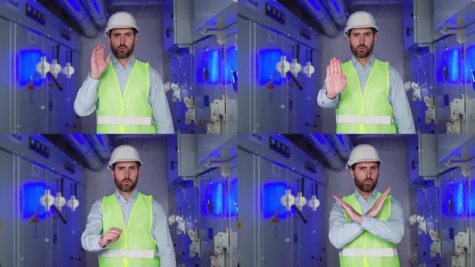 戴白色安全帽的男性电气工程技术工人的肖像，变电所工人在蓝光、高压和故障电气设备的背景下示意停车。