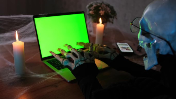 穿着骷髅装的男人深夜在笔记本电脑上打字写一篇可怕的文章聊天，发派对邀请