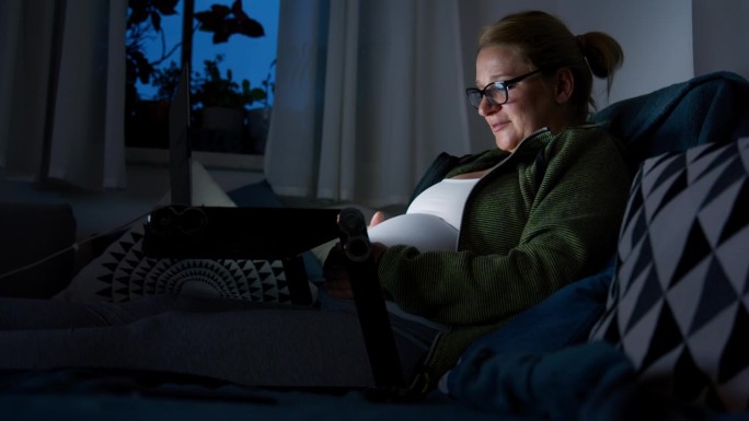 孕妇晚上用笔记本电脑在沙发上按摩肚子