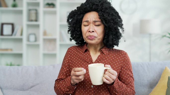 关闭了。生病的非裔美国女性坐在家里客厅的沙发上咳嗽。她得了感冒、病毒、支气管炎或流感